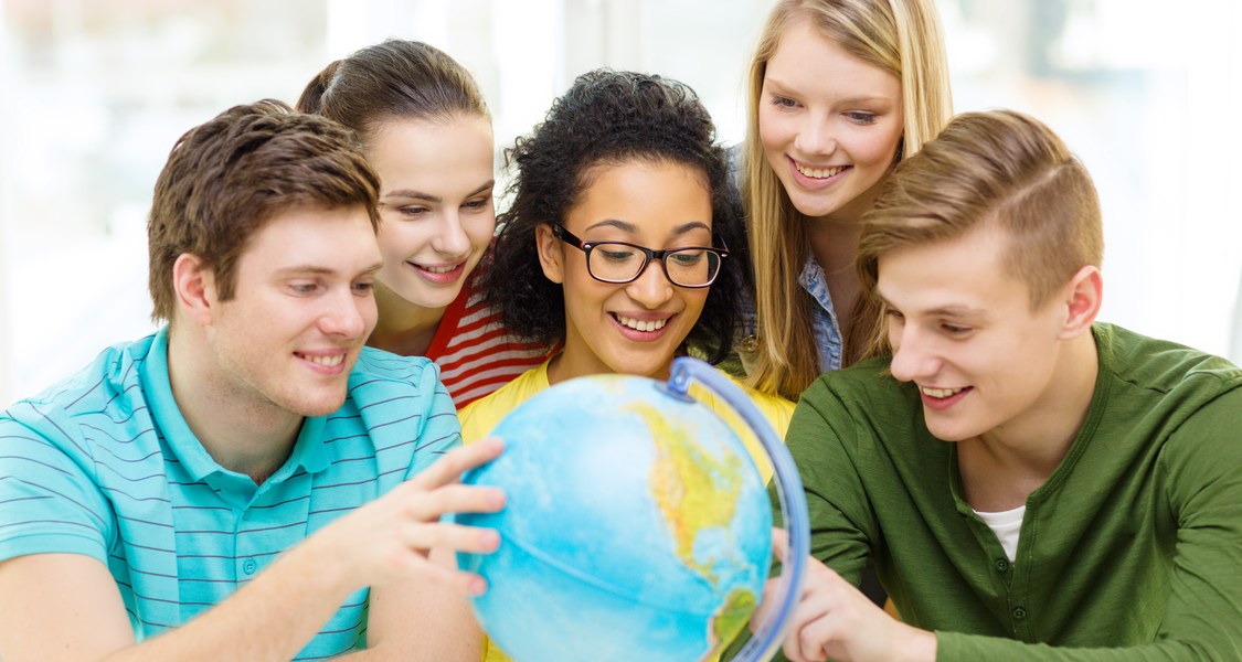 Fünf Studierende sitzen um einen Globus herum und zeigen auf verschiedene Länder.