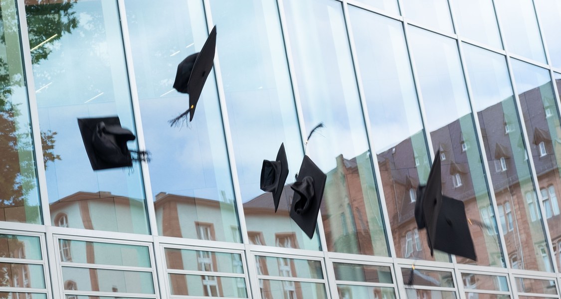 Vor der Universitätsbibliothek in Marburg fliegen mehrere Hüte von Absolvierenden in die Höhe.