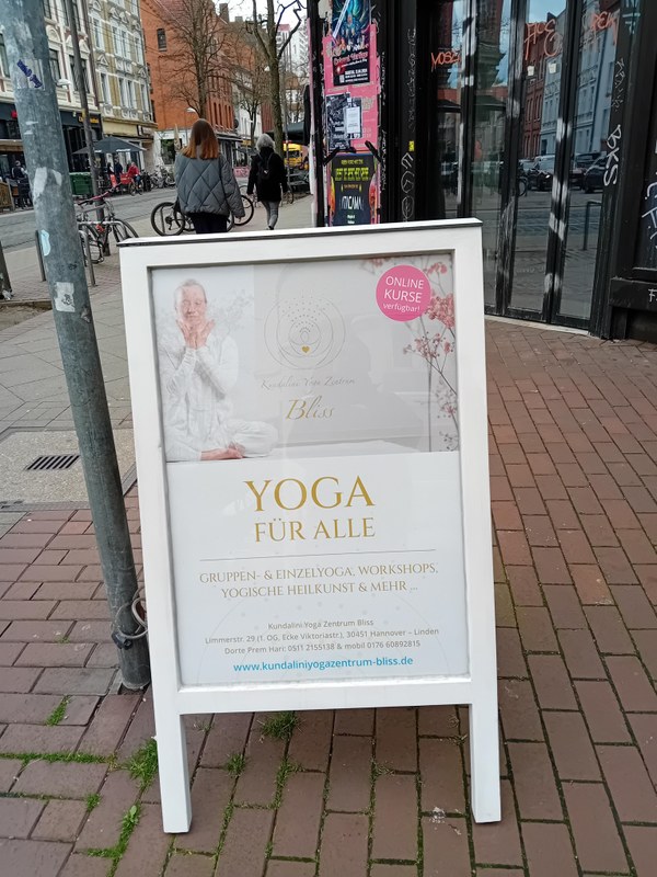 Das Foto zeigt einen Aufsteller auf der Limmerstraße in Hannover. Zu sehen ist ein Plakat mit Werbung für ein Yoga-Studio und symbolisiert die Präsenz von Yoga-Studios im urbanen Raum.