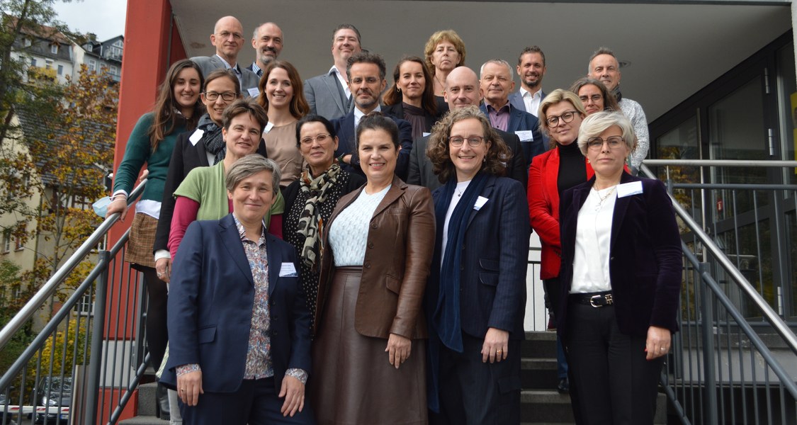 The Participants of the Rectors' Meeting of the EUPeace Network pose for a Picture. They are standing next to each other on stairs, facing the camera. The picture was taken outside, the weather was cloudy.