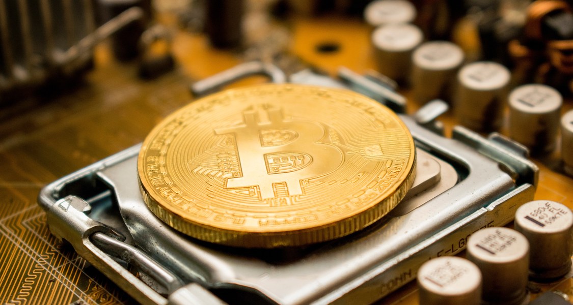 A large gold coin with the BitCoin-logo placed on a CPU.