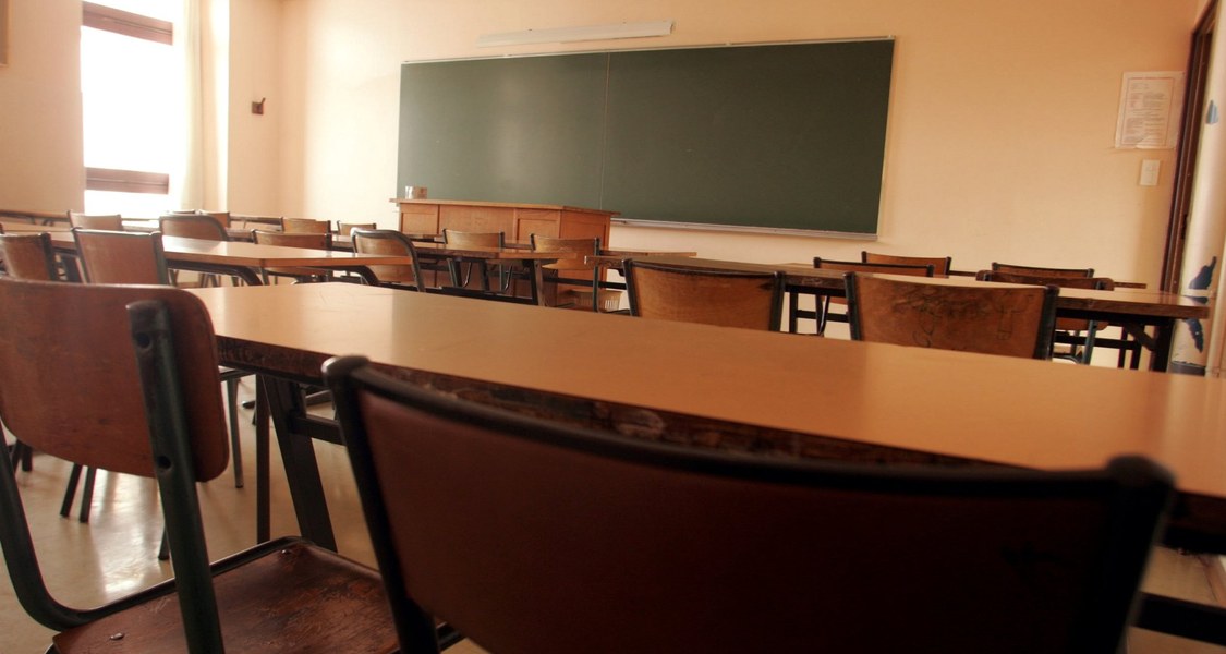 An empty classroom with wooden tables and chairs and a blackboard.