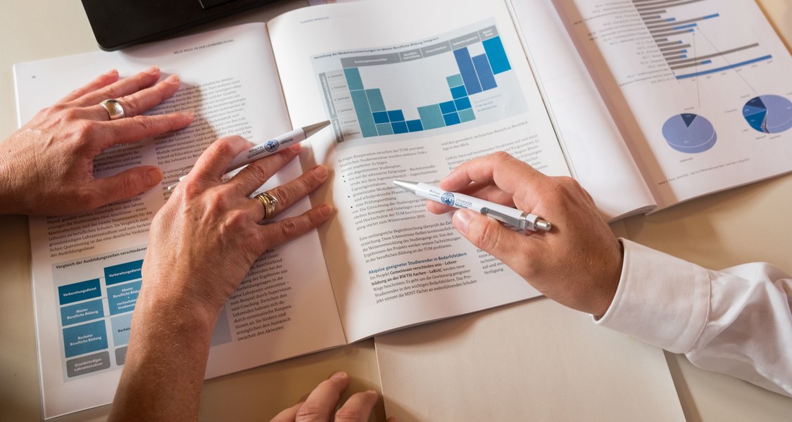 Document on a table with four hands on it, two of them holding pens