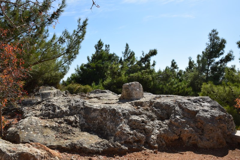 A rock with a roughly hewn altar on top sits among Mediterranean undergrowth