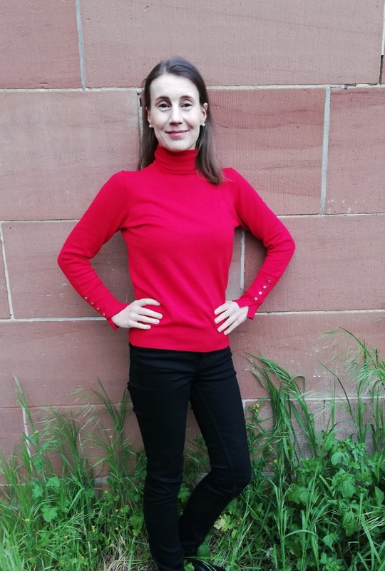 A full-length portrait of Mirja Biehl standing in front of a brick wall