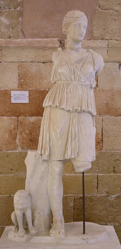 A partly broken statue depicting the goddess Artemis, standing with a dog at her feet