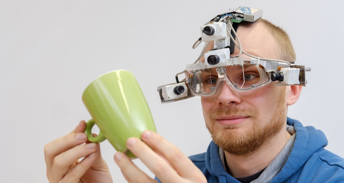 A person with an eye tracker holds a cup in his hands and looks at it
