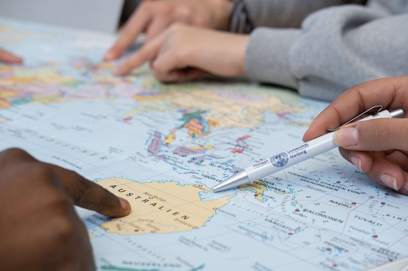 Different fingers point to various locations on a world map.
