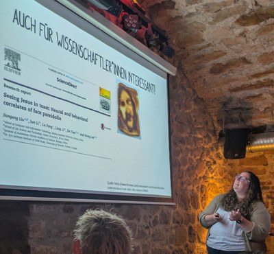 The picture shows Tina Meller giving a talk in the context of the Pint of Science Festival addressing the question why we investigate healthy people for a better understanding of mental diseases.