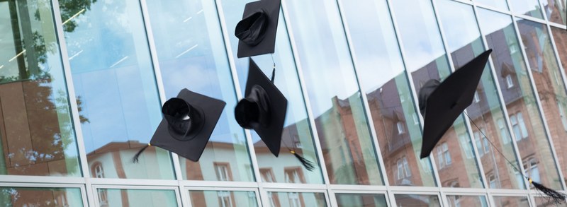 Doctor´s hats thrown in the air in front of the glass facade of the university library in Marburg.