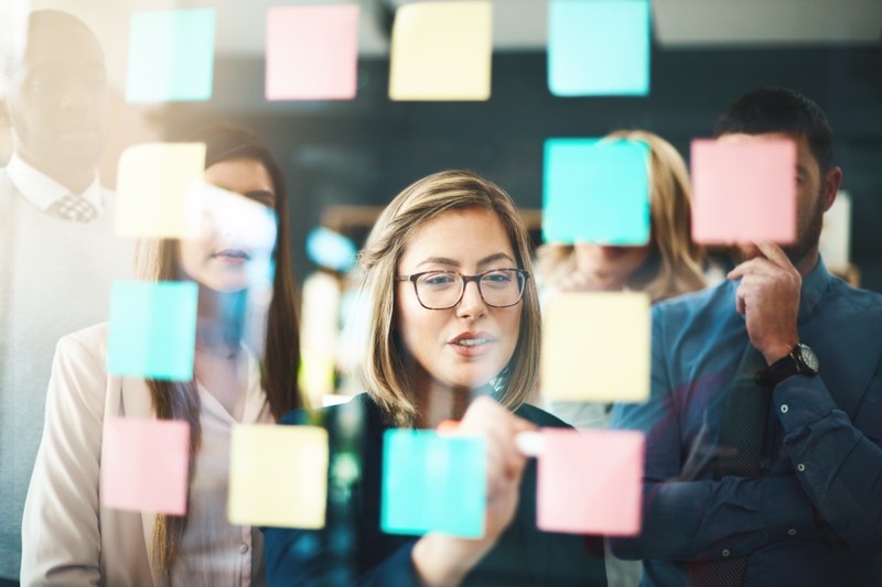 Several persons standing in front of a whiteboard with post-its.