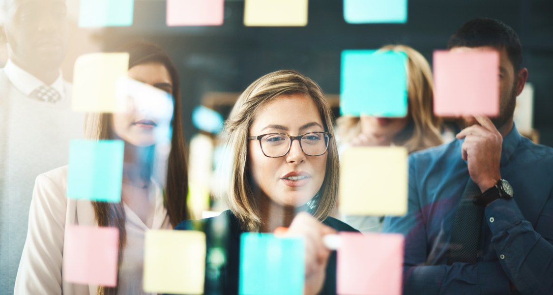 Several persons standing in front of a whiteboard with post-its.